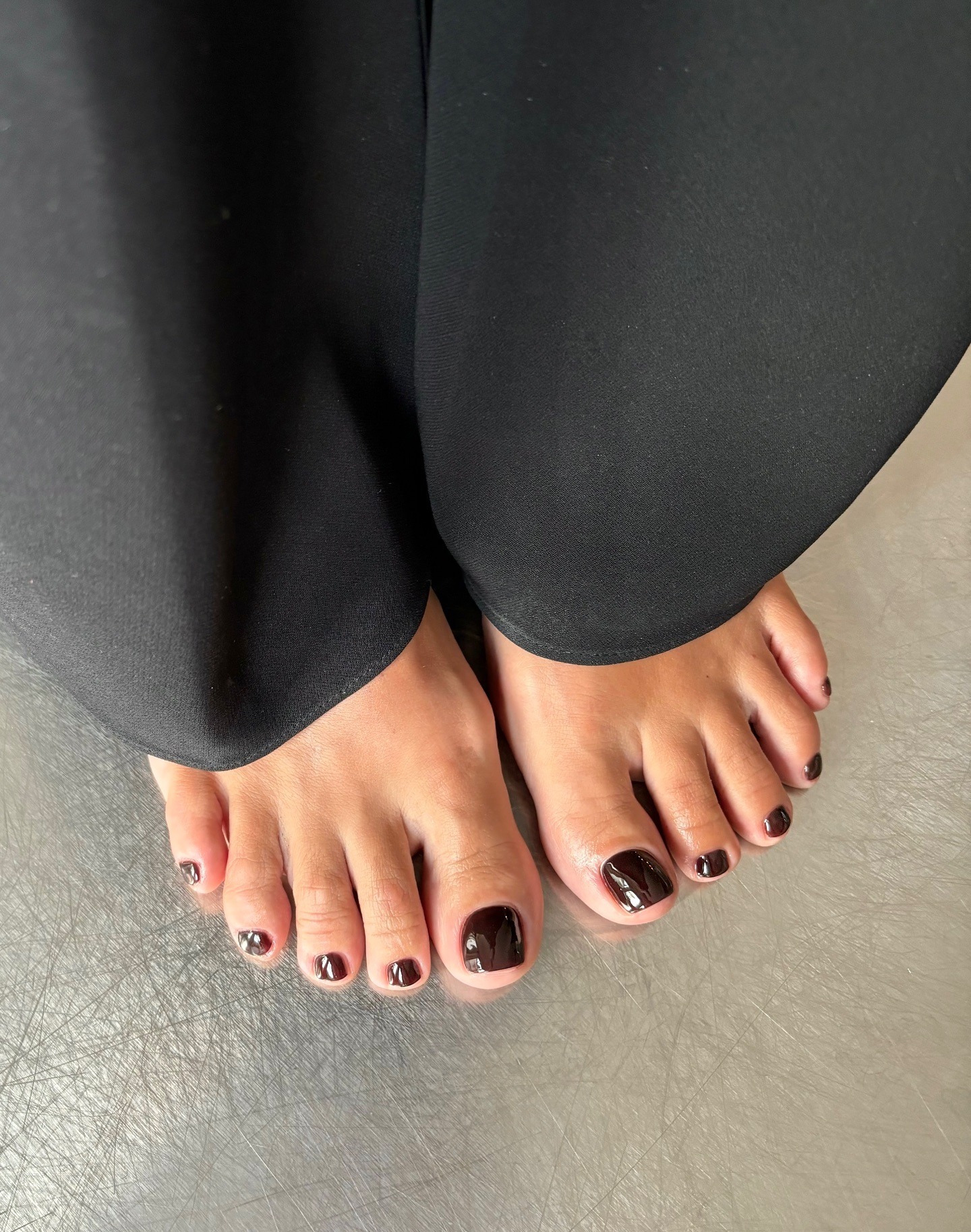 A woman's feet on a silver floor with a burgundy pedicure