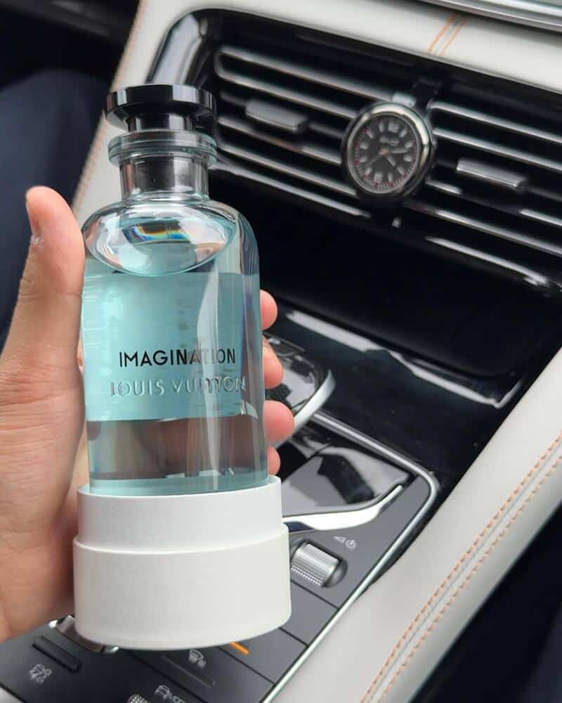 holding a bottle of Louis Vuitton Imagination Cologne