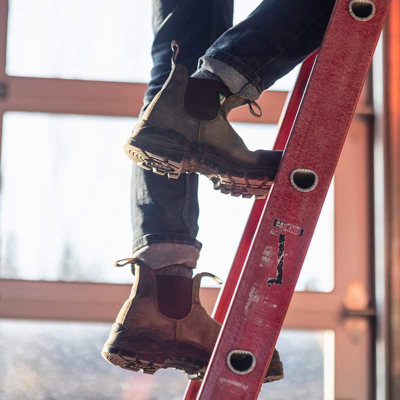man climbing a ladder wearing a pair of Blundstone boots