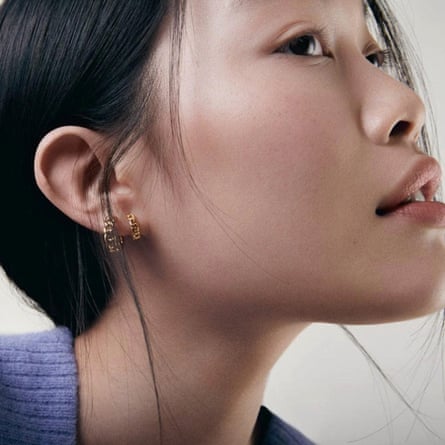 A woman wearing gold Orelia Mini Chain Huggie Hoop Earrings